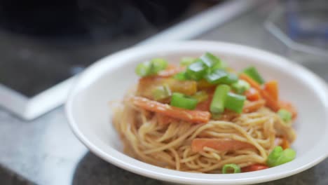 Spaghetti-noodles-with-colorful-sliced-cooked-peppers,-carrots-and-fresh-leek-with-peanut-sauce-on-a-whit-plate-steaming