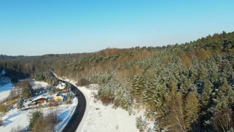 Cars-driving-over-a-black-asphalt-road-which-is-cleared-from-white-snow-between-a-streched-green-forest-on-a-bright-day-near-Gdansk-Poland
