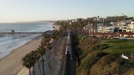 Flying-over-railroad-at-sunset,-San-Clemente-Pier-Beach,-California,-aerial-wide-slow-motion-shot