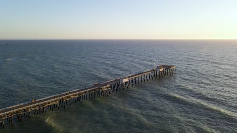 Flying-over-the-pier-at-sunset,-San-Clemente-Pier-Beach,-California,-aerial-wide-slow-motion-shot