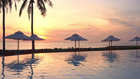 A-colorful-sunset-on-the-ocean-horizon-reflects-on-a-resort-swimming-pool-and-beach