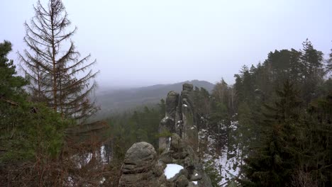 outlook-on-a-sandstone-rock-formation-in-Prachov-Rocks,-Bohemian-Paradise,-in-winter-with-flying-snowflakes,-pan-left