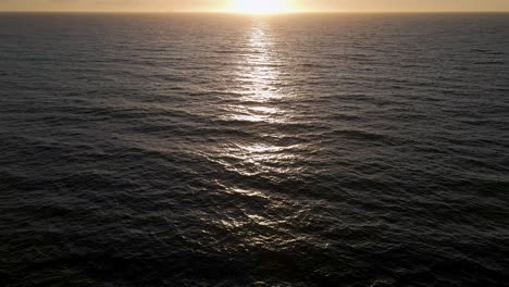 Sunset-over-Pacific-Ocean,-aerial-tilt-up-reveal-of-sun-setting-over-sea-horizon