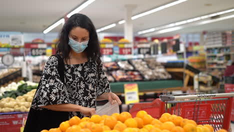 Young-Latina-woman-wearing-a-face-mask-checks-oranges-for-freshness-at-a-grocery-store