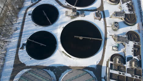 Top-down-aerial-of-water-basins-and-tilting-up,-revealing-sewage-treatment-plant-in-winter