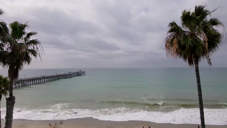 An-aerial-drone-shot-flying-over-San-Clemente-State-Beach,-California,-towards-the-San-Clemente-Pier-on-a-cloudy-day