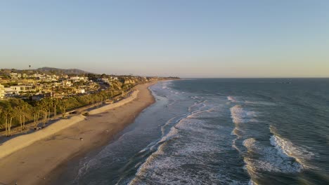 Aerial-view-of-beautiful-ocean-with-empty-sandy-beach,palm-trees-and-promenade-during-sunset
