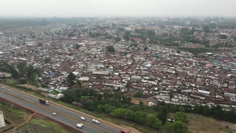 Aerial-view,-Kibera-slum-and-highway-traffic-with-Nairobi-Kenya-in-misty-skyline,-pull-back-drone-shot
