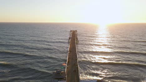 Aerial-drone-shot-flying-directly-over-the-top-of-San-Clemente-Pier,-California,-during-sunset-and-clear-sky