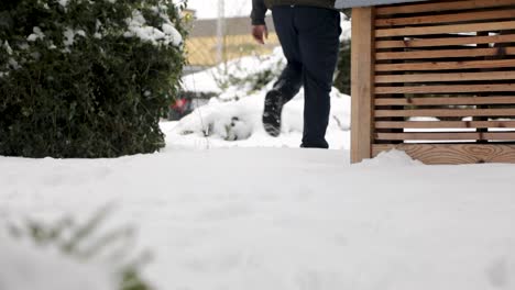 Low-angle-slowmotion-of-person-walking-through-deep-snowy-garden-after-strong-snowfall-in-winter