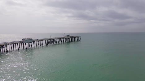 Cinematic-aerial-view-of-pier-into-the-ocean-on-calm-overcast-day