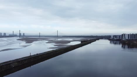 Aerial-across-River-Mersey-Runcorn-low-tide-canal-entrance-old-town-waterfront-orbit-left