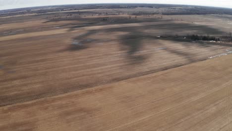 Shadows-from-clouds-on-brown-farm-fields-seen-from-drone-overhead
