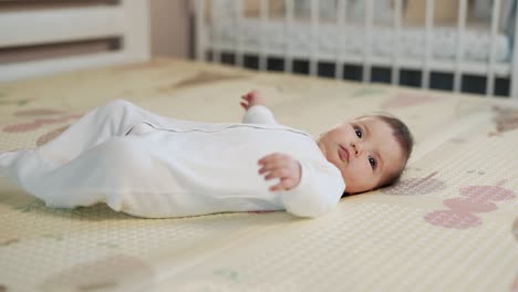 Side-view-of-a-little-baby-girl-lying-on-her-back-on-a-thermal-mat
