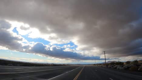 Driving-along-an-almost-empty-highway-in-the-Mojave-Desert-with-ominous-and-dramatic-clouds-overhead---point-of-view