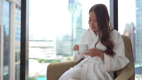 Woman-in-bathrobe-drinks-coffee-and-looks-out-of-window