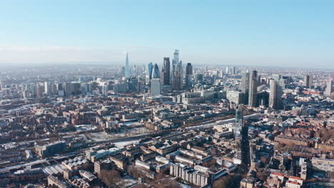 high-dolly-back-drone-shot-over-city-of-london-skyscrapers-from-tower-hamlets-clear-day-after-snow