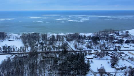 Aerial-drone-footage-of-a-small-town-overlooking-a-frozen-Lake-Erie-in-Western-New-York-State-during-winter-with-fresh-snowfall-and-ice