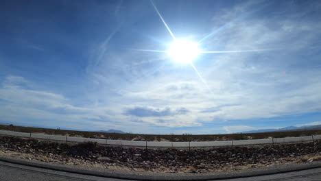 Wir-Reisen-Entlang-Eines-Mojave-Wüsten-Highways-Mit-Einer-Hellen-Sonne-über-Uns-Und-Joshua-Bäumen,-Die-Die-Trockene-Landschaft-Markieren