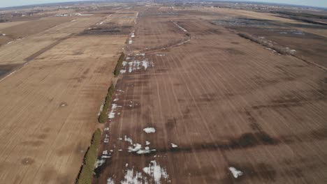 Long-open-farm-fields-in-Spring-with-patches-of-snow-on-brown-landscape