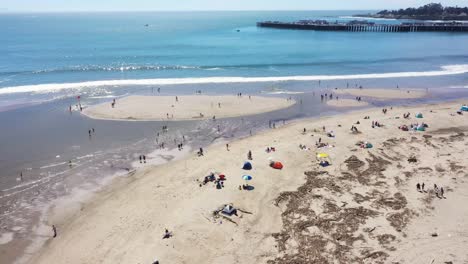 Drone-flyover-of-Santa-Cruz,-CA-beach-with-people-relaxing-and-playing-in-the-water