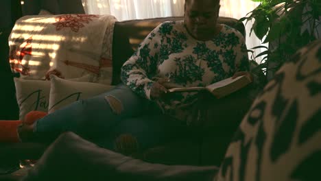 Mujer-Negra-Relajándose-En-El-Sofá-Leyendo-La-Biblia