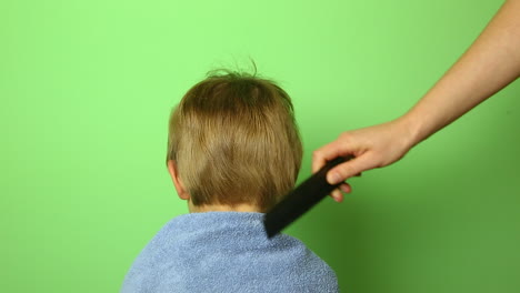 Woman-hand-comb-small-boy-blond-hair,-head-close-up-isolated-on-green-background