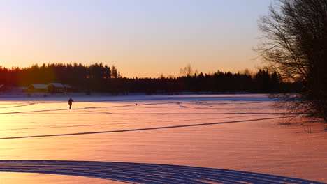 Erstaunlicher-Sonnenuntergang-über-Der-Winterlandschaft,-Während-Frau-Und-Hund-Auf-Dem-Zugefrorenen-See-Wandern