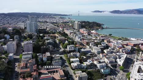 Long-drone-shot-in-San-Francisco-flying-over-Fisherman's-Wharf-area-towards-Maritime-Plaza-and-Ghirardelli-Square-with-the-Golden-Gate-Bridge-in-the-background