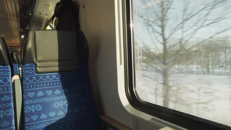 Empty-window-seat-in-train,-white-snowy-winter-landscape-passing-by