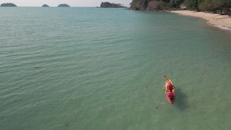 slow-motion-aerial-drone-view-of-people-kayaking-close-to-a-tropical-beach-with-islands-in-distance