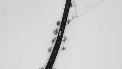 Aerial-Shot-Of-Car-Driving-On-Road-In-Natural-Winter-Landscape,-Snow-Covered-Country
