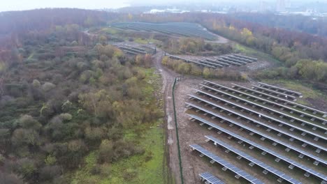 Solar-panel-array-rows-aerial-view-misty-autumn-woodland-countryside-rising-tilt-up