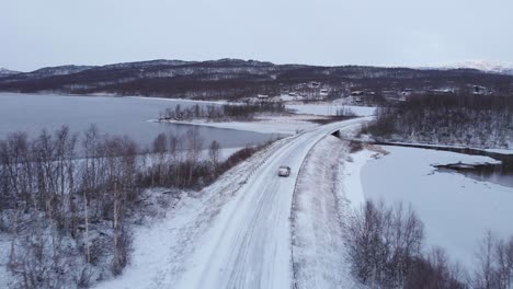 Car-crossing-Snowy-desolate-Road-amidst-nordic-setting---Tracking-Aerial-shot