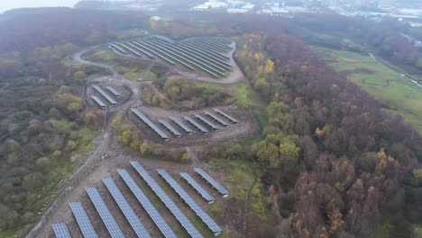 Solar-panel-array-rows-aerial-view-misty-autumn-woodland-countryside-high-pan-right