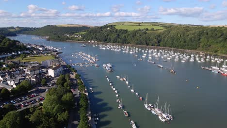 Aerial-over-Dart-river-in-Kingswear,-Devon-w-UK,-many-sailing-boats-on-the-river-in-the-middle-of-the-green-shore