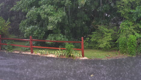 A-heavy-rain-falling-on-the-driveway-outside-during-a-thunderstorm-with-a-spilt-rail-fence-in-the-background
