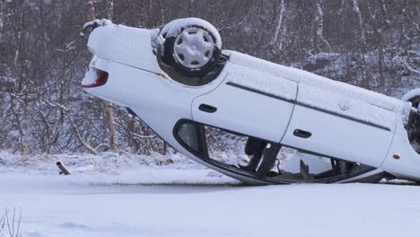 Car-upside-down-in-a-serious-accident-on-a-frozen-and-snowy-road-amidst-nordic-forest---Static-medium-shot