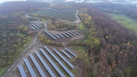 Solar-panel-array-rows-aerial-view-misty-autumn-woodland-countryside-slow-descending-shot