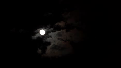 Moon-glowing-through-clouds-on-dark-night-black-sky-timelapse