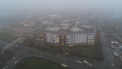 Misty-foggy-hospital-building-UK-town-traffic-aerial-view-pull-back-high-angle