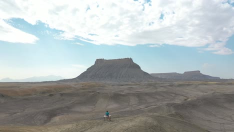 Surreal-Aerial-Scenery,-DJ-Playing-Music-on-Grey-Sandstone-Hill,-Utah-Desert-USA-Pull-Back-Drone-Shot