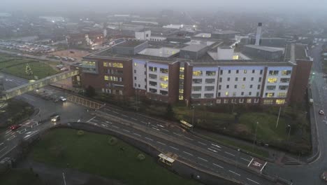 Aerial-view-British-NHS-hospital-on-misty-wet-damp-morning-high-to-low-descend