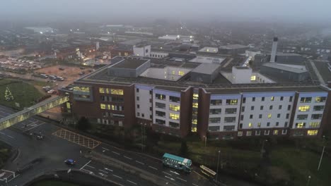 Aerial-view-British-NHS-hospital-on-misty-wet-damp-morning-rising-above-rooftop