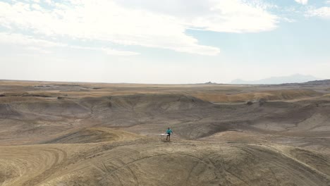 Orbit-Drone-Aerial-View-of-Lonely-DJ-Playing-Music-in-Dry-Desert-Landscape,-Utah-USA-with-Factory-Butte-Natural-Landmark-in-Background,-Drone-Shot