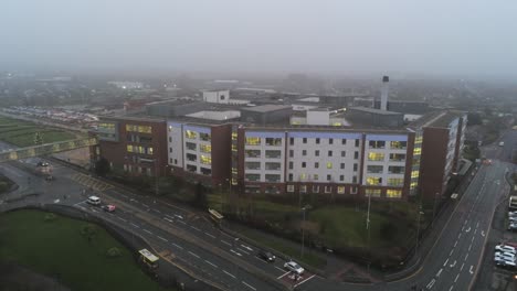 Misty-foggy-hospital-building-UK-town-traffic-aerial-view-rising-above-rooftop