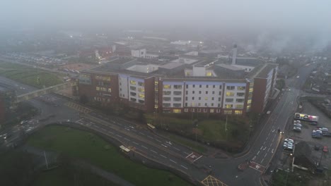 Misty-foggy-hospital-building-UK-town-traffic-aerial-view-lowering-tilt-up