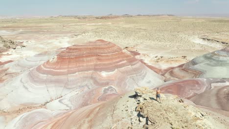 Lonely-Shirtless-Man-Walking-on-Peak-in-Dry-Desert-Mars-Look-Alike-Landscape-on-Hot-Summer-Day,-Drone-Aerial-View