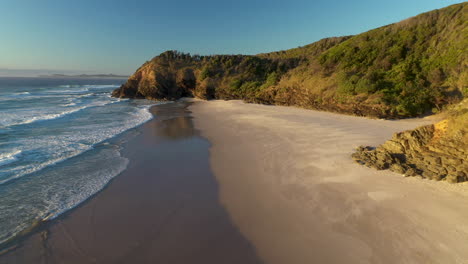 Rotating-drone-shot-of-man-walking-along-sandy-beach-at-Broken-Head-near-Byron-Bay