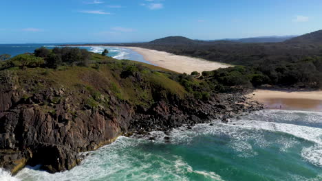 Cinematic-fly-over-of-coastal-rock-outcropping-revealing-beautiful-sandy-beach-at-Cabarita-Beach-Australia